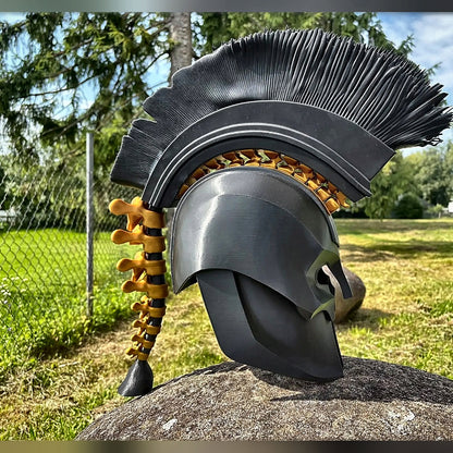 Black Greek warrior helmet with tall black crest and gold spine, outdoors on a rock