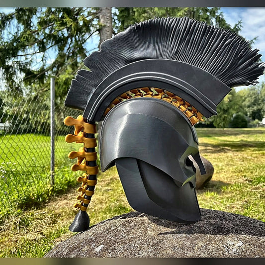 Black Greek warrior helmet with tall black crest and gold spine, outdoors on a rock