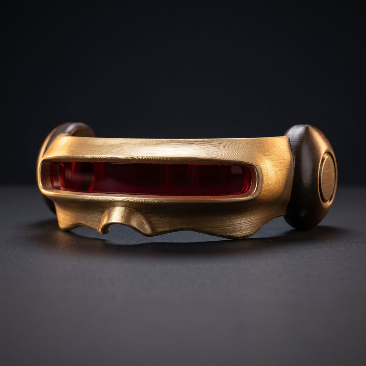 Gold Cyclops visor cosplay prop with deep red lens, front three-quarter view on a dark studio surface