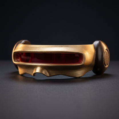 Gold Cyclops visor cosplay prop with deep red lens, front three-quarter view on a dark studio surface