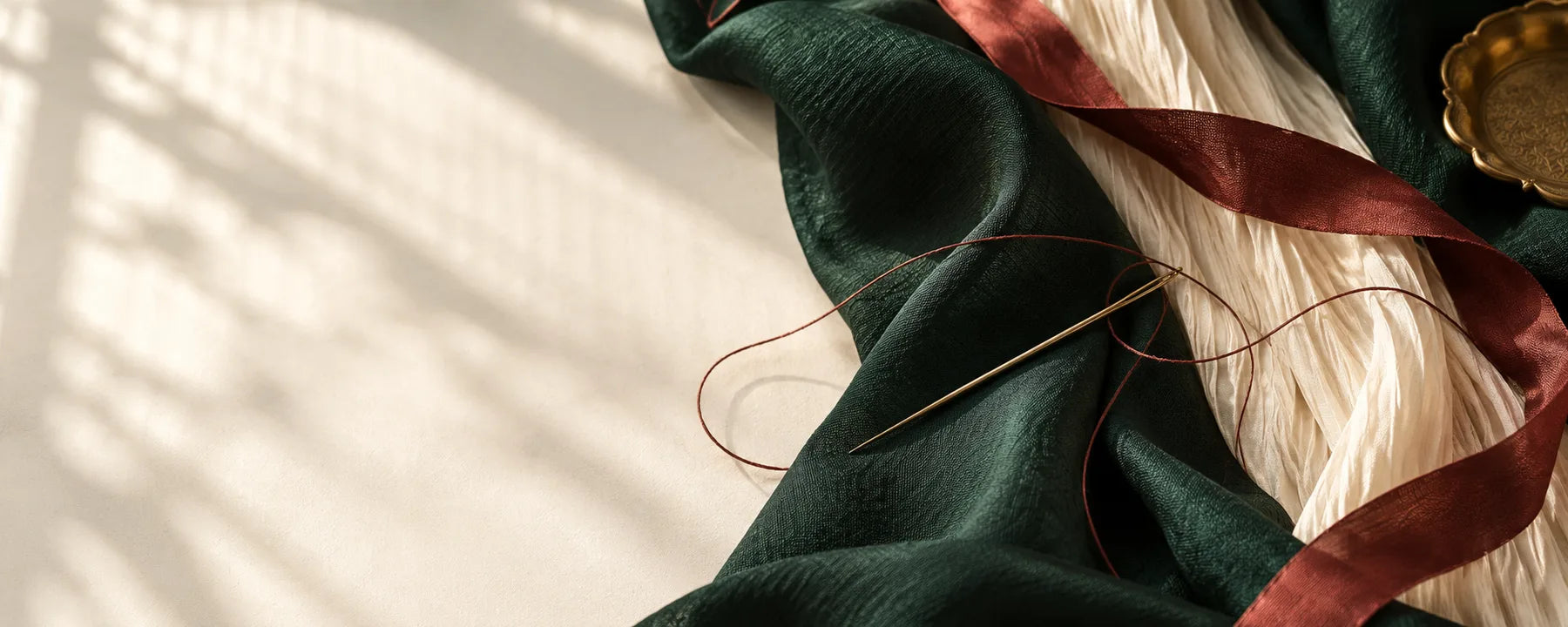 Forest green and ivory fabrics, burgundy ribbon and tailoring tools — brand still life
